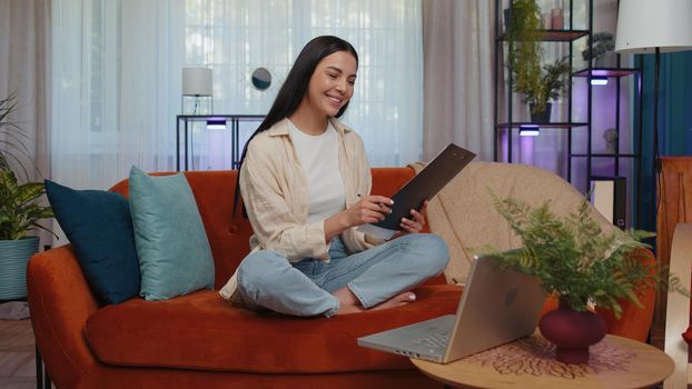 Girl accountant working with financial graph documents, calculate taxes for charts and graph reports of home income on couch. Young businesswoman working on laptop computer, planning expenses budget