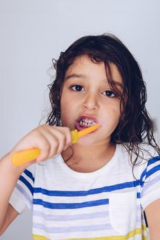 vertical portrait of a little girl brushing her teeth in the bathroom in the morning after taking a shower, kids hygiene concept, copy space for text