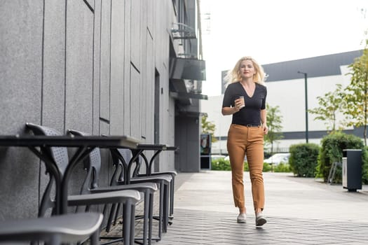 Cheerful fashionable blonde holding coffee outdoors.