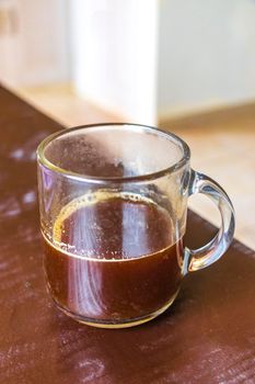 Glass cup of black coffee from Mexico on wooden background in clean kitchen.