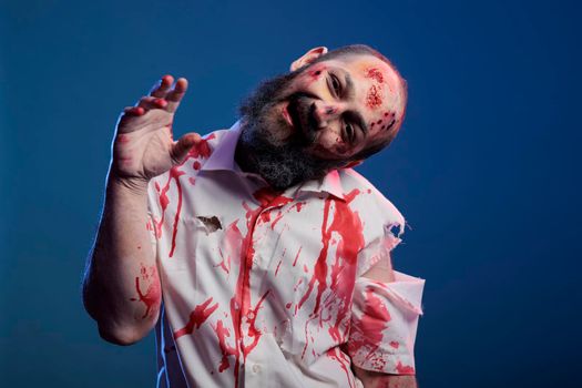 Spooky halloween zombie looking crazy evil, having blood on shirt and dangerous aggressive bloody look. Eerie apocalyptic corpse with ugly dirty scars and wounds, brain eating demon.