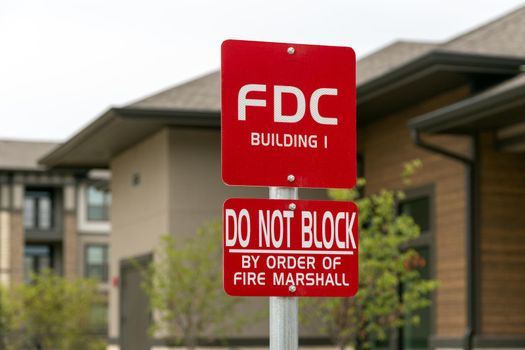 Information sign with inscription: FDC Building 1, do not block by order of fire marshal, trees and bulding on background