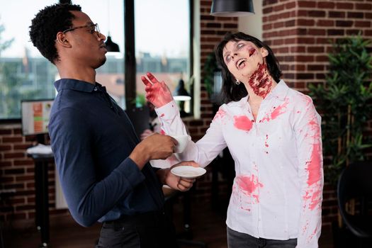 Aggressive zombie chatting with man in office, brain eating monster with bloody scars and ugly wounds being in startup business workplace. Woman evil corpse talking to businessman.