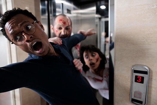 Frightened adult running from cruel walkers escaping office elevator, brain eating walking dead monsters attacking man in terror and massacre. Being scared and afraid after bloody zombies attack.
