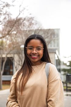 Vertical portrait of happy and smiling black teen girl outdoors looking at camera. Copy space. Education and gen z concept.