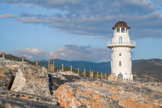 White port lighthouse on the background of mountains and sky and clouds.