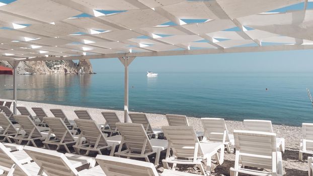 Empty sun loungers under a canopy on the beach. The beach area is empty. No people. White plastic sunbeds under the sun shade. The holiday season ends. Holiday season begins. Waiting for tourists