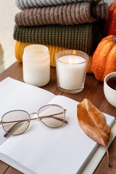 Hello fall. Cozy warm image. High angle view opened blank book for mockup design with sweaters and candles