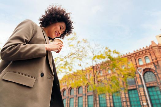 successful business woman smiles walking by the street with a coffee in her hand, concept of urban lifestyle, copy space for text