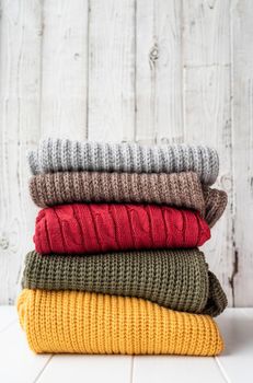 Hello fall. Cozy warm image. Stack of autumn warm sweaters on white wooden background