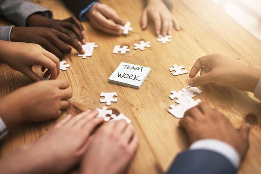 Each piece is as important as the next. High angle shot of a group of unrecognizable coworkers building a puzzle on their boardroom table