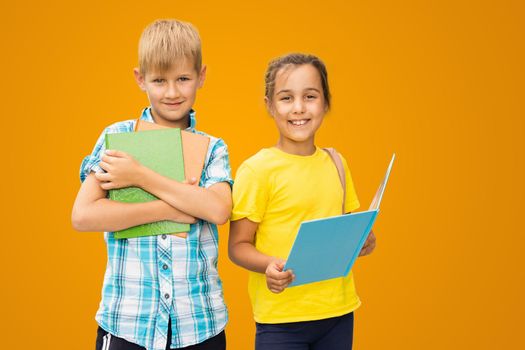 Photo of two small girl boy schoolchildren brother sister classmates hold books isolated orange color background.