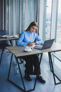 The secretary checks the schedule. Cheerful young beautiful woman in glasses with a smile uses a laptop while sitting at her workplace