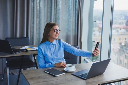 Smart female employee with netbook looking at camera during mobile call, successful freelancer in jacket talking on phone via app