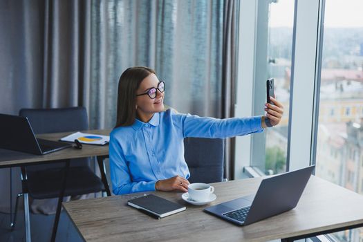Smart female employee with netbook looking at camera during mobile call, successful freelancer in jacket talking on phone via app
