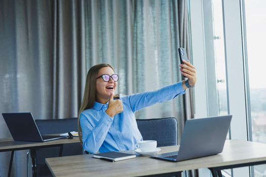 Smart female employee with netbook looking at camera during mobile call, successful freelancer in jacket talking on phone via app