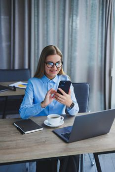 Smart female employee with netbook looking at camera during mobile call, successful freelancer in jacket talking on phone via app