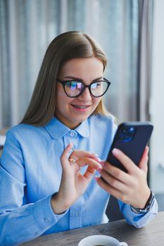 Smart female employee with netbook looking at camera during mobile call, successful freelancer in jacket talking on phone via app