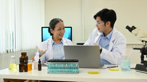 Senior female biotechnology specialist supervisor and her assistant conducting experiment in a laboratory.