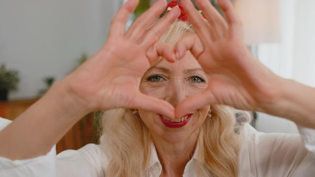 I love you. Senior grandmother makes symbol of love, showing heart sign to camera, express romantic feelings, express sincere positive feelings. Charity, gratitude, donation. Woman close-up happy face