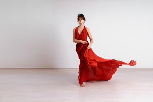 Dancer in a red flying dress. Woman ballerina dancing on a white studio background.