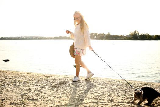 Young blonde, woman, girl walking on the beach in spring in a dress and white sweater with a cat on a sunny day