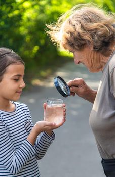 A child and grandmother examines the water with a magnifying glass. Selective focus. People.