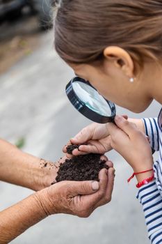 The child examines the soil with a magnifying glass. Selective focus. Kid.