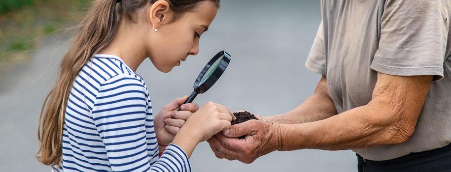 The child examines the soil with a magnifying glass. Selective focus. Kid.