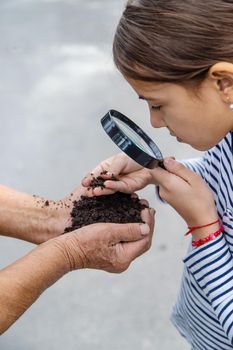 The child examines the soil with a magnifying glass. Selective focus. Kid.