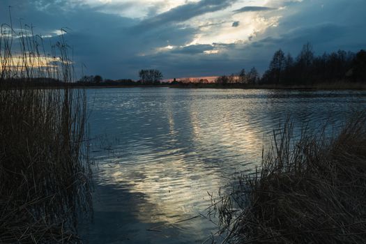 Dark evening clouds over the lake and light reflection in the water, spring view
