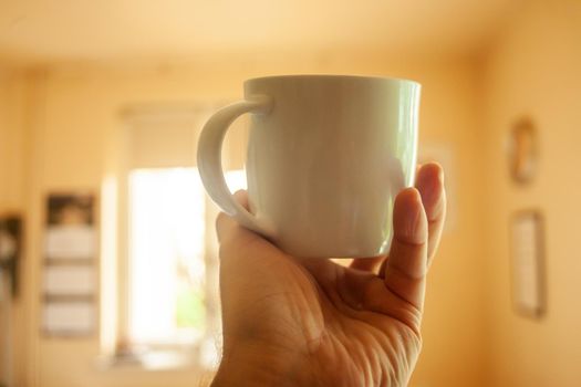 A white cup in the man hand and the daylight from the window