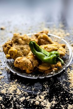 Famous Aloo pakora/ aloo bhajia in a glass plate with green chili and some chickpea flour spread on a surface.Shot of alu bhajiya on a transparent glass plate. Vertical shot.