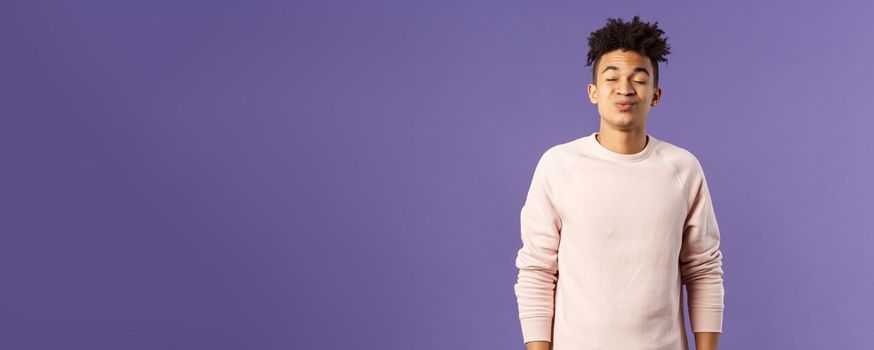 Portrait of cute and silly, young hispanic trying to kiss girl after date for the first time, leaning with folded lips and closed eyes towards her, making funny smile, standing purple background.