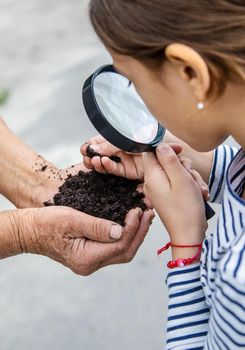 The child examines the soil with a magnifying glass. Selective focus. Kid.