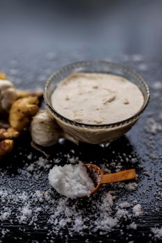 Shot of freshly ground garlic and ginger paste in a glass bowl on a black surface along with raw ginger, and some garlic with salt on sprinkle on the surface. Lasan adrak ka paste in a glass bowl on wooden surface.