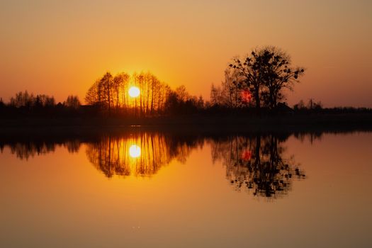 The reflection in the water of the sunset behind the trees, spring evening view