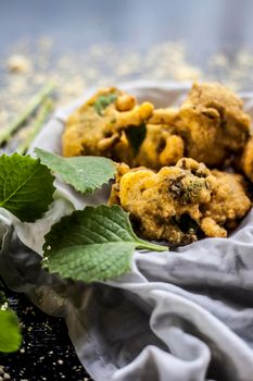 Close up shot of monsoon snack ajwain pakora in a container along with some fresh ajwain leaf with it on a surface with some sprinkled chickpea flour with all the ingredients required to make pakora.