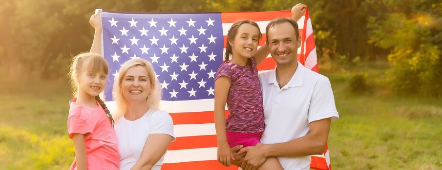 Patriotic holiday. Happy family, mother and daughters with American flag outdoors on sunset. USA celebrate independence day 4th of July