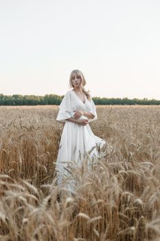 A blonde woman in a long white dress walks in a wheat field. The concept of a wedding and walking in nature.