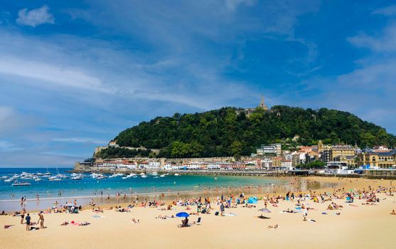 Landscape of La Concha beach in the city of San Sebastian, in the Spanish Basque Country, on a sunny day with people enjoying the beach and Mount Urgull in the background.