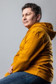 Portrait of proud handsome Caucasian man looking away with prideful and pensive face, sitting on chair, wearing urban style hoodie. Indoor studio shot isolated on gray background.