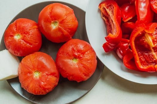 Boiled tomatoes on a plate with sliced red pepper, top view