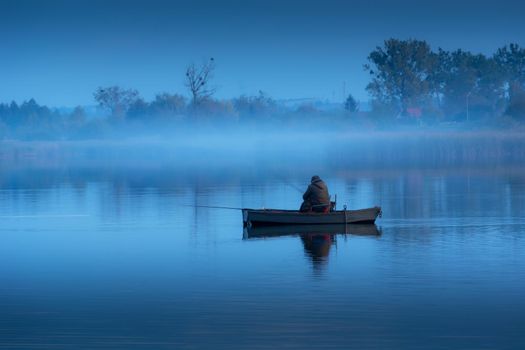 Angler in a boat and fog on a calm blue lake