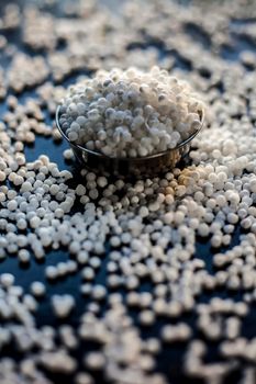 Close up shot of raw sago pearls or tapioca pearls in a glass plate on a black colored surface.