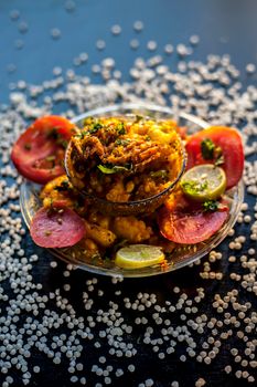 Close up shot of spicy tasty sabudana khichdi or sago ball khichdi along with some sliced tomatoes, some cut lemons in a glass plate, and raw sago balls.