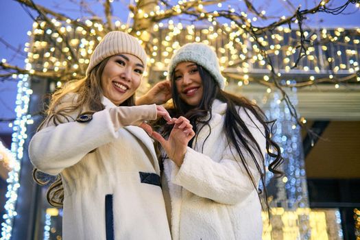 Two girlfriends asian girls in white coats are having fun, showing heart, hugging, new year, light bulbs