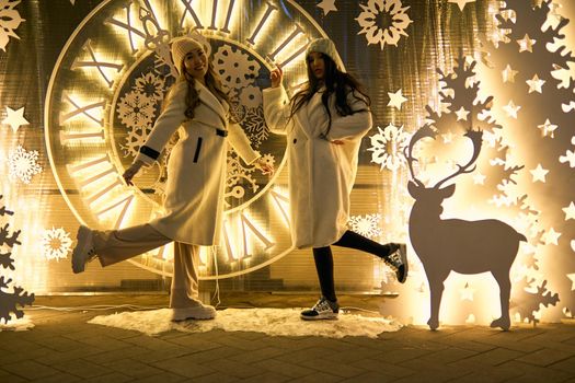 Two girlfriends asian girls in white coats are having fun hugging, new year, light bulbs