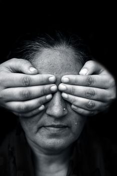 Modern creative shot of a lady with hands closing her lips and expressing see no evil isolated on black background in black and white colors.