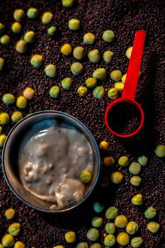 Skin booster in a bowl along with green peas, mustard seeds and some yogurt on black surface.